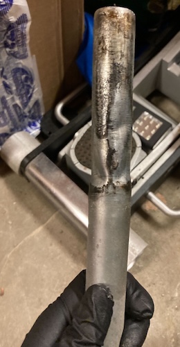 The seat post is gripped in my gloved hand. You can see that the metal is dinged and warped in many places.